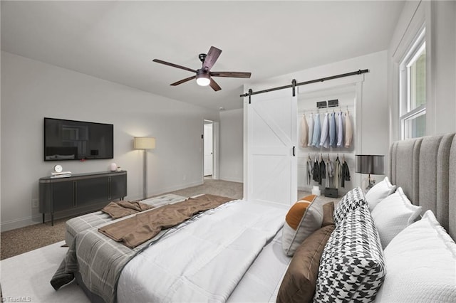 carpeted bedroom with a walk in closet, a barn door, a closet, baseboards, and ceiling fan