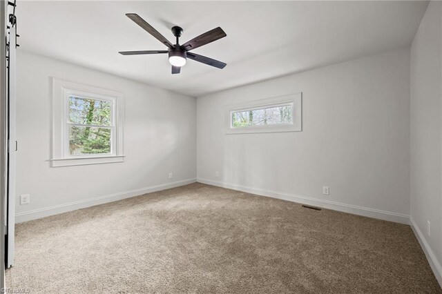 spare room with carpet flooring, baseboards, visible vents, and a wealth of natural light