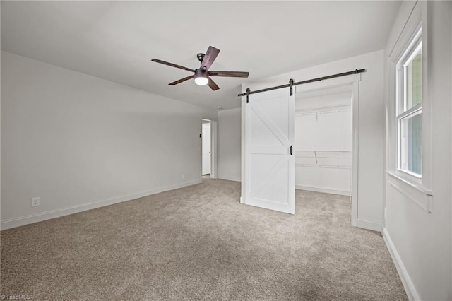 unfurnished bedroom with a barn door, a closet, carpet, baseboards, and a spacious closet