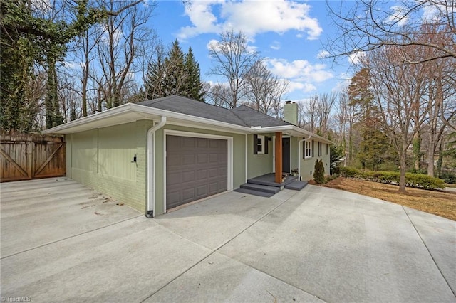 view of front of home featuring driveway, fence, an attached garage, brick siding, and a chimney