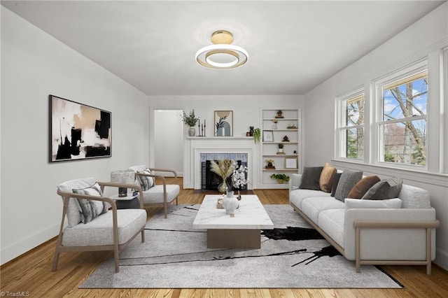 living area with built in features, a tile fireplace, baseboards, and wood finished floors