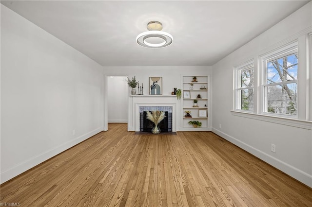 unfurnished living room with light wood-style flooring, a fireplace, baseboards, and built in shelves