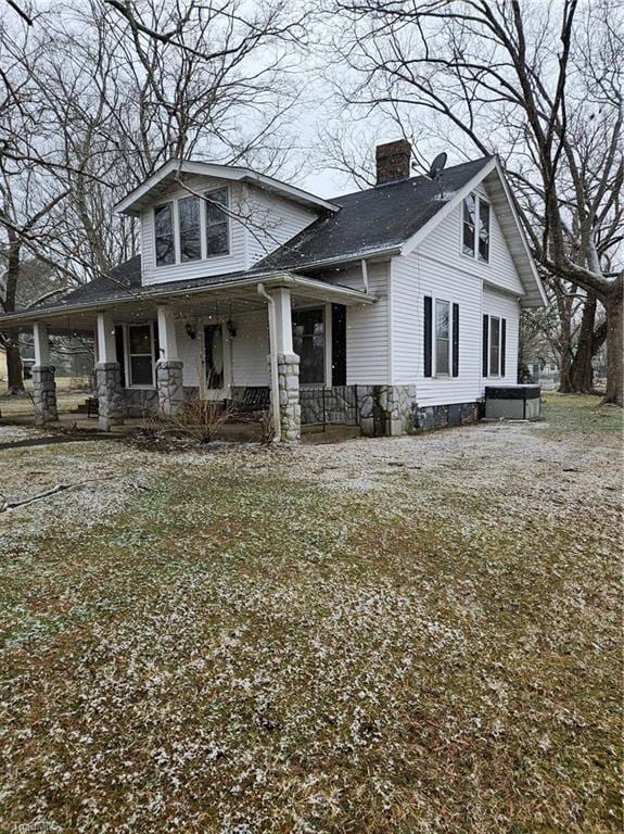 view of front facade featuring a porch, stone siding, a chimney, and a front lawn