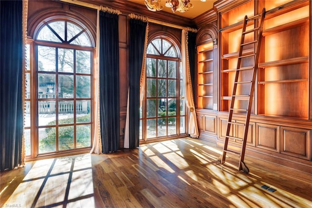 doorway to outside with ornamental molding, wooden walls, a chandelier, and hardwood / wood-style floors