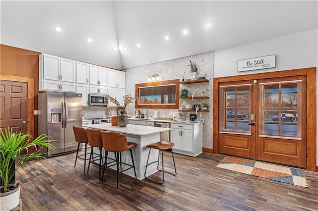 kitchen featuring white cabinetry, high vaulted ceiling, stainless steel appliances, a center island, and a kitchen bar