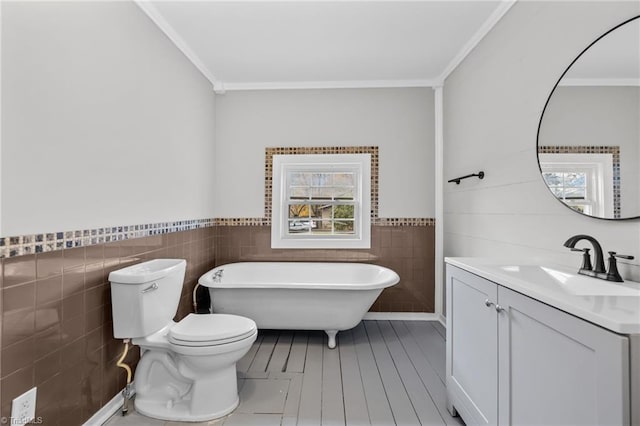 bathroom with a washtub, toilet, ornamental molding, and tile walls