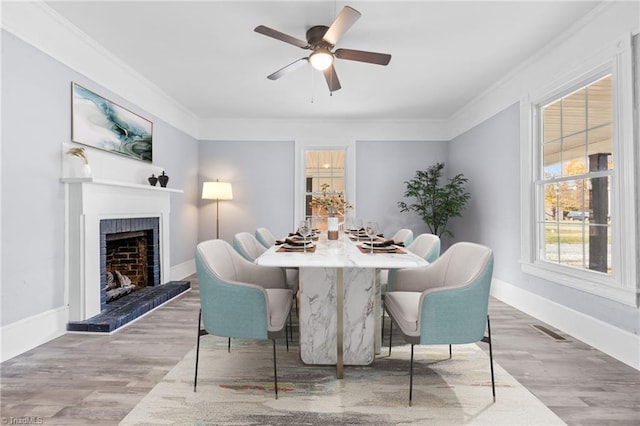 dining space featuring a brick fireplace, ceiling fan, ornamental molding, and light wood-type flooring