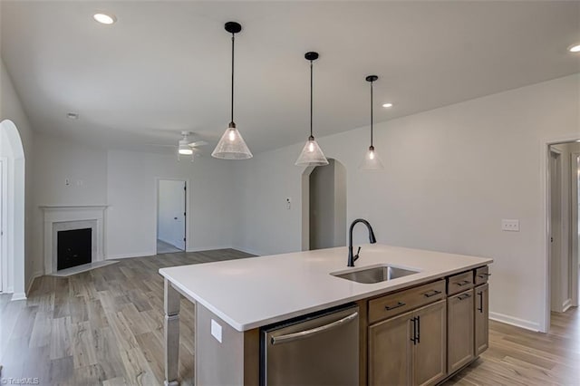 kitchen featuring arched walkways, light countertops, light wood-style floors, a sink, and dishwasher