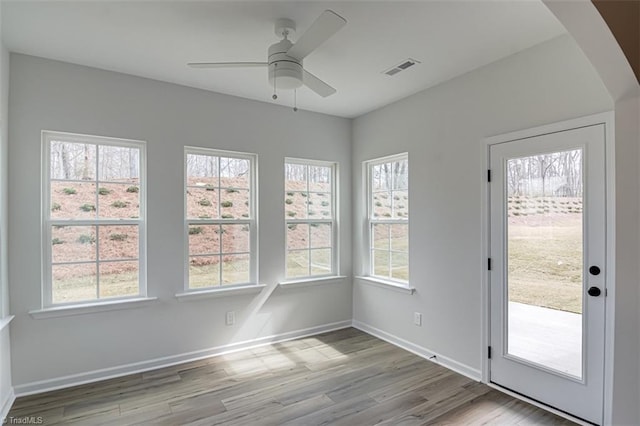 unfurnished sunroom featuring a healthy amount of sunlight, ceiling fan, and visible vents