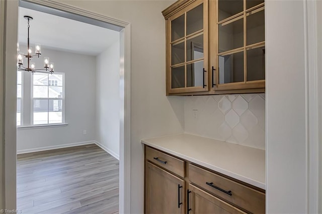 kitchen with tasteful backsplash, baseboards, glass insert cabinets, and light wood finished floors