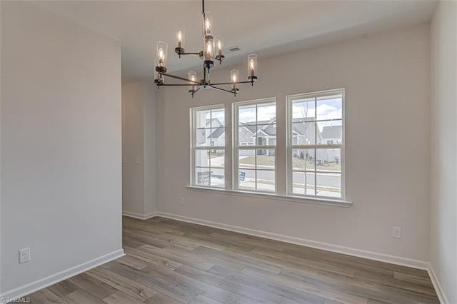 unfurnished room with a chandelier, a healthy amount of sunlight, baseboards, and wood finished floors