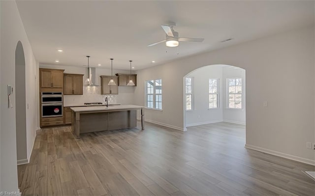 kitchen with wall chimney exhaust hood, arched walkways, and open floor plan