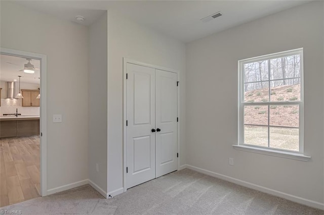 unfurnished bedroom with a closet, light carpet, baseboards, and ensuite bathroom