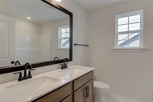 full bath featuring toilet, double vanity, baseboards, and a sink