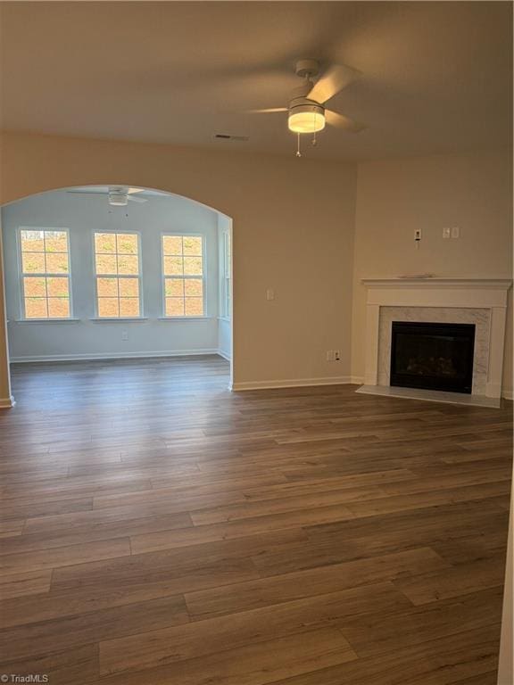 unfurnished living room featuring plenty of natural light, arched walkways, a fireplace, and ceiling fan