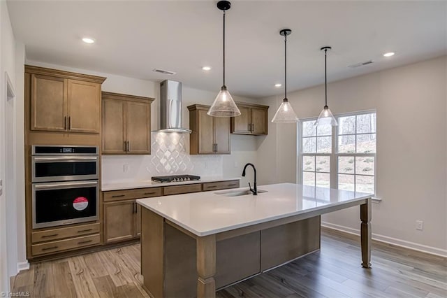 kitchen with double oven, gas stovetop, a sink, visible vents, and wall chimney exhaust hood