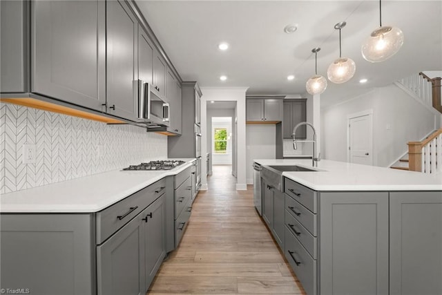 kitchen featuring gray cabinets, pendant lighting, sink, light wood-type flooring, and stainless steel appliances