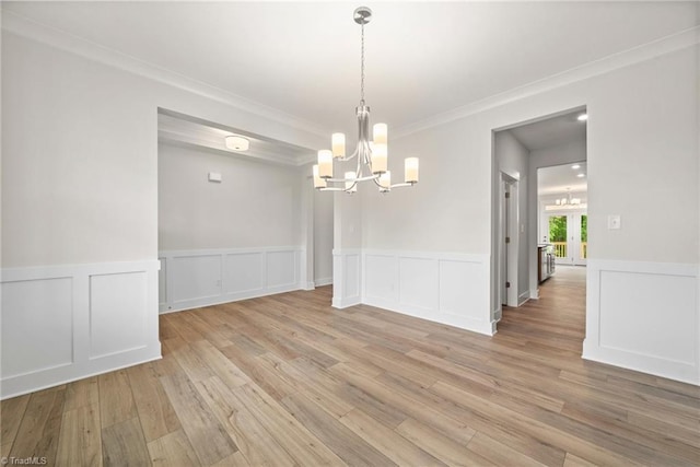 unfurnished dining area featuring light wood-type flooring, crown molding, and a chandelier