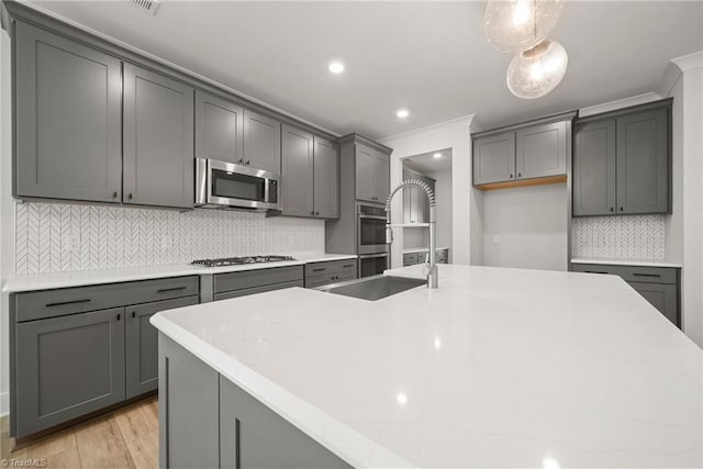 kitchen featuring appliances with stainless steel finishes, tasteful backsplash, hanging light fixtures, a kitchen island with sink, and gray cabinetry