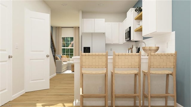 kitchen with light wood finished floors, stainless steel microwave, white fridge with ice dispenser, white cabinetry, and open shelves