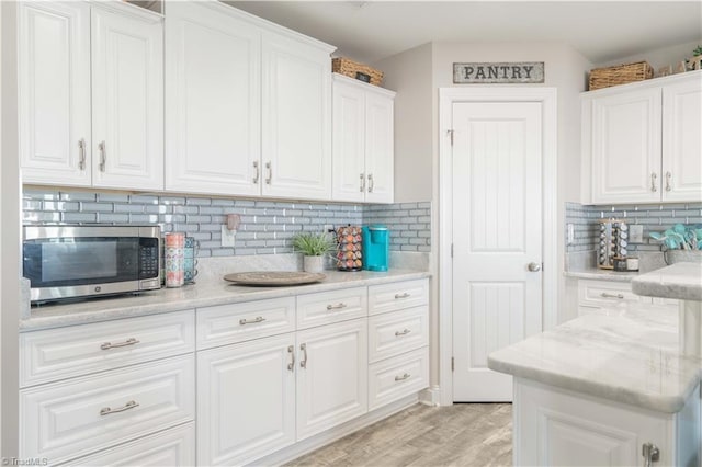 440 Sportsman Dr, Salisbury, NC 28146 - kitchen with stainless steel microwave, white cabinetry, decorative backsplash, light wood-style flooring, and light stone countertops