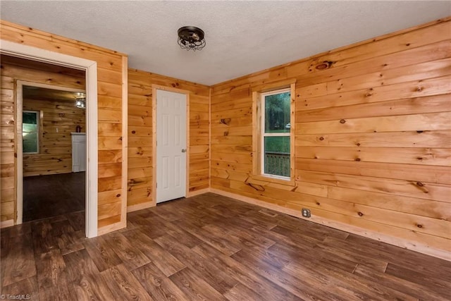 unfurnished room with ceiling fan, a textured ceiling, wood walls, and dark hardwood / wood-style flooring