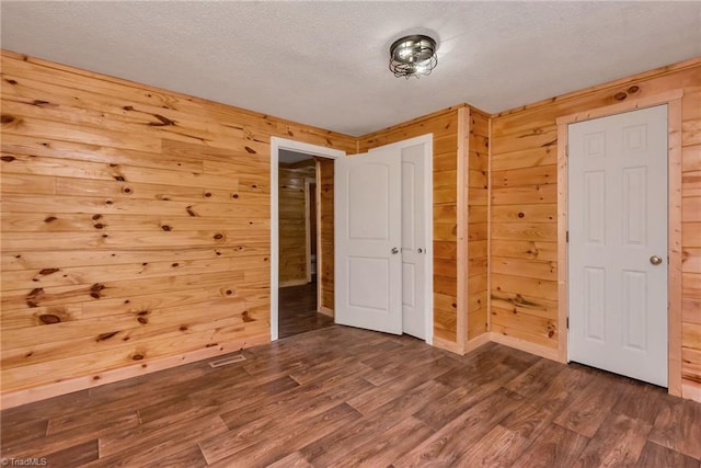 unfurnished bedroom with a textured ceiling, wooden walls, and dark hardwood / wood-style flooring