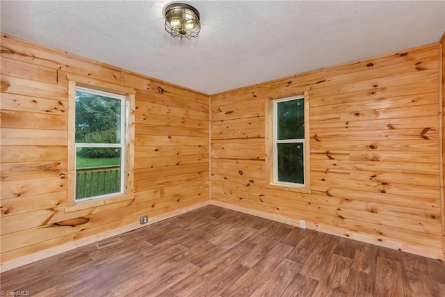 unfurnished room with wood-type flooring, a textured ceiling, and wood walls