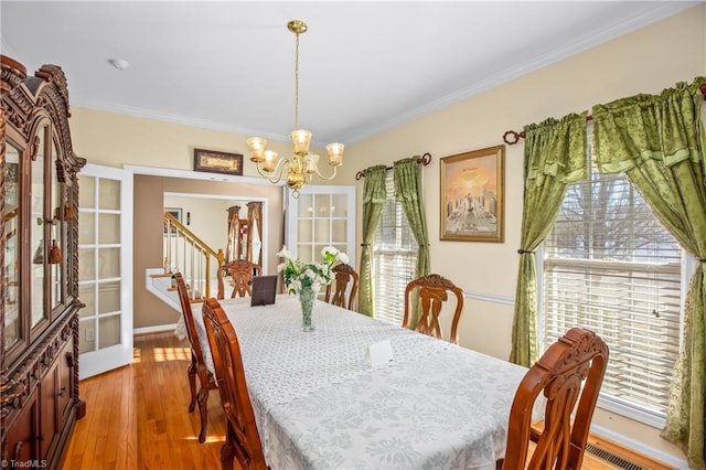 dining area with ornamental molding, light hardwood / wood-style floors, and an inviting chandelier