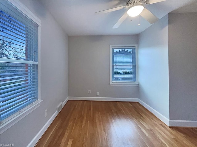 spare room featuring a ceiling fan, visible vents, baseboards, and wood finished floors