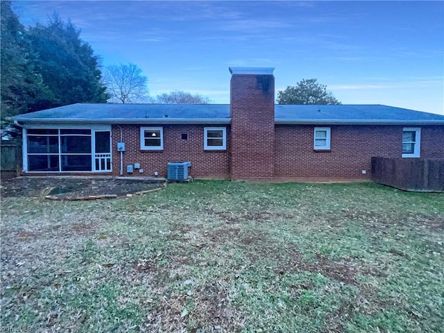 back of property featuring brick siding, a chimney, a lawn, a sunroom, and central AC