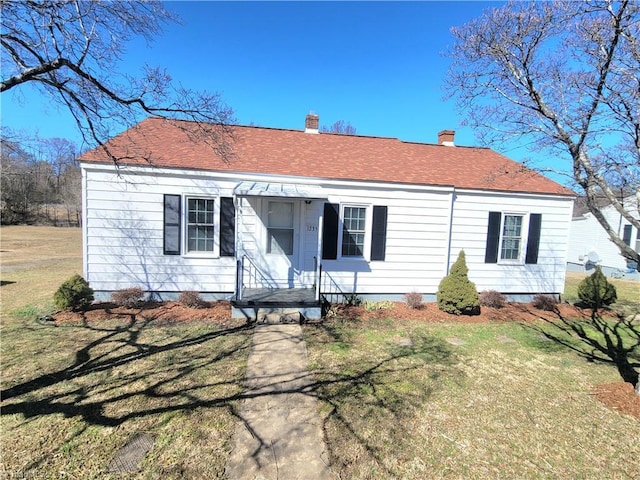 view of front of property featuring a shingled roof, a chimney, and a front yard