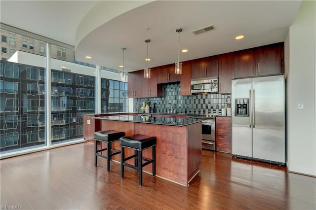 kitchen with decorative backsplash, a kitchen island, visible vents, appliances with stainless steel finishes, and dark wood-type flooring