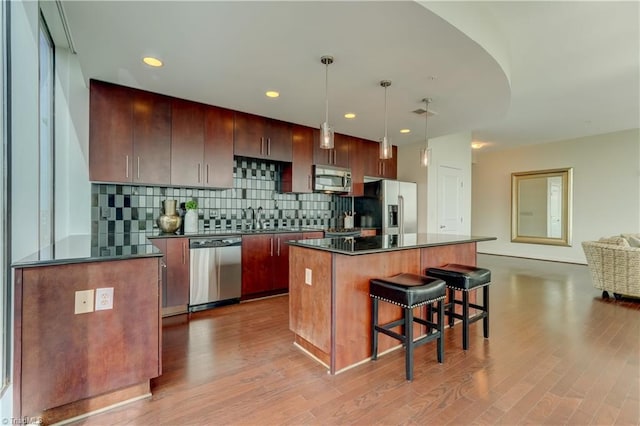 kitchen featuring decorative backsplash, a kitchen island, a kitchen bar, light wood-style floors, and stainless steel appliances