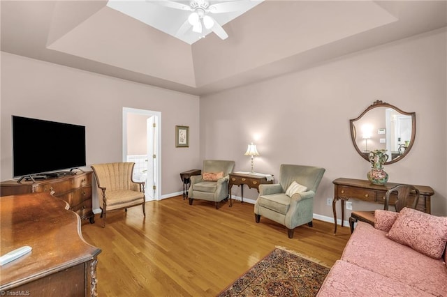 living area featuring baseboards, light wood-type flooring, a tray ceiling, and a ceiling fan