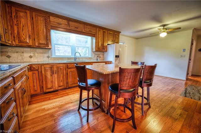 kitchen with white refrigerator with ice dispenser, a kitchen island, light wood-type flooring, a kitchen bar, and a sink