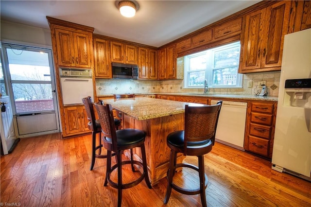 kitchen featuring white appliances, light stone counters, brown cabinets, a center island, and light wood-type flooring