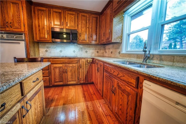 kitchen with brown cabinetry, white appliances, a sink, and light stone countertops