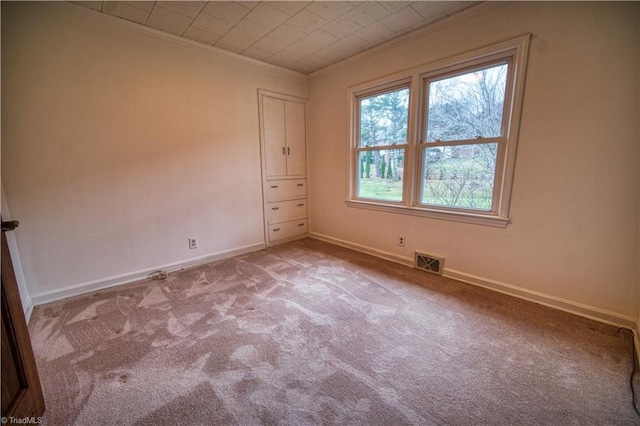 unfurnished room with baseboards, light carpet, visible vents, and crown molding