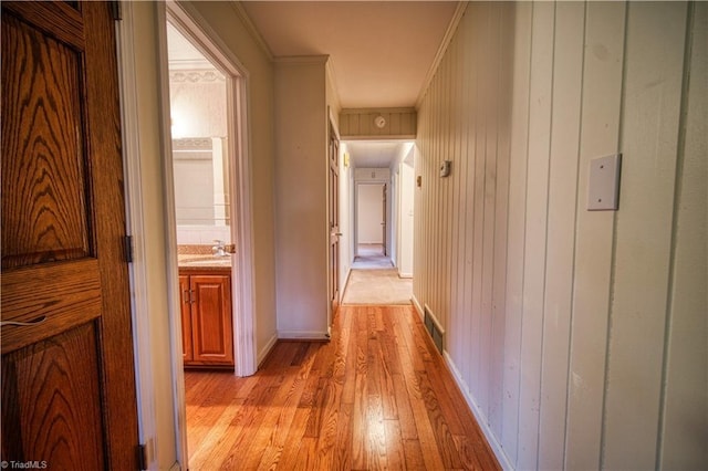 hall with baseboards, visible vents, ornamental molding, light wood-style floors, and a sink