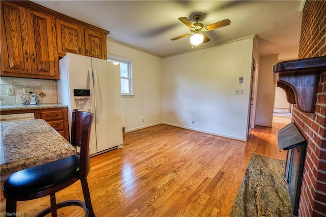 kitchen featuring white appliances, decorative backsplash, brown cabinetry, crown molding, and light wood-type flooring