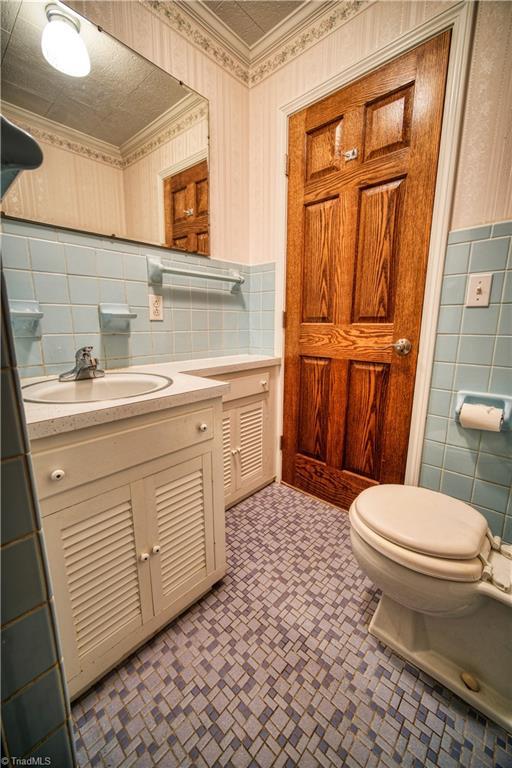 bathroom with toilet, wallpapered walls, ornamental molding, and tile walls