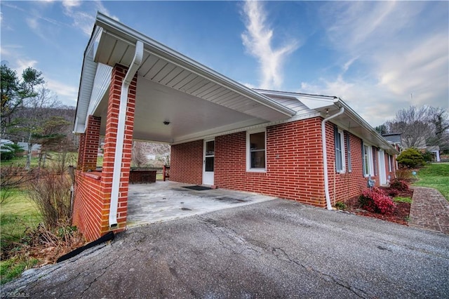 view of property exterior with a carport, brick siding, and driveway