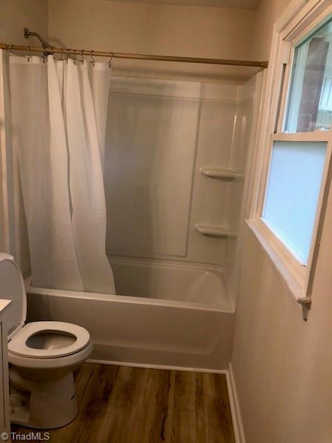 full bath with shower / tub combo, toilet, wood finished floors, vanity, and plenty of natural light