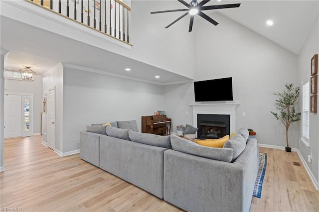 living room with ceiling fan with notable chandelier, light wood-type flooring, high vaulted ceiling, and a wealth of natural light