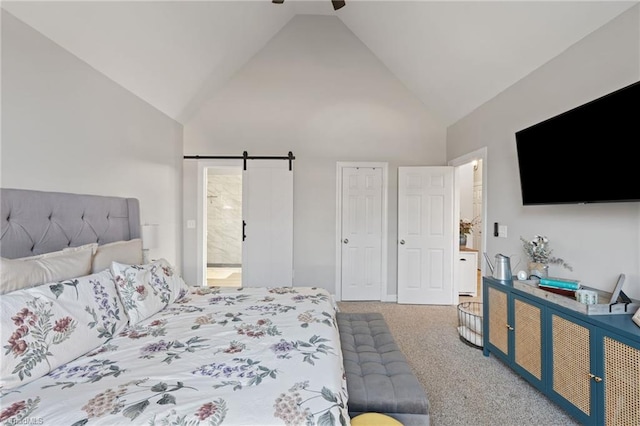 carpeted bedroom with a barn door, ceiling fan, ensuite bath, and high vaulted ceiling