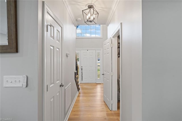 hallway with a chandelier, light wood-type flooring, and ornamental molding