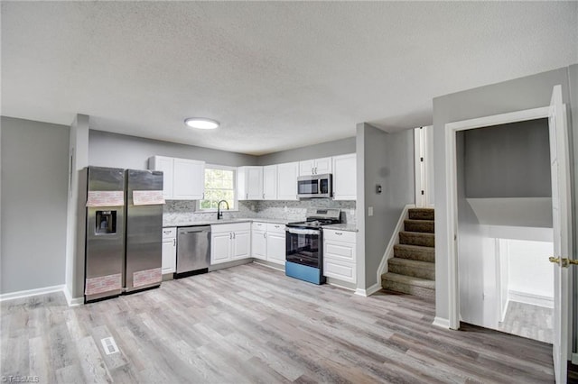 kitchen featuring white cabinets, a textured ceiling, sink, light wood-type flooring, and appliances with stainless steel finishes