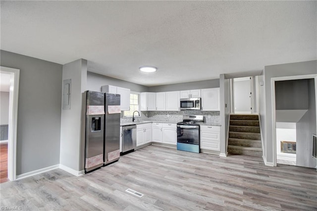 1638 Colonial Dr, Salisbury, NC 28144 - kitchen with stainless steel appliances, light countertops, white cabinetry, light wood-style flooring, and tasteful backsplash