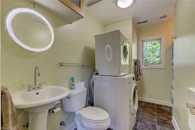 bathroom featuring stacked washer / dryer, visible vents, baseboards, toilet, and ornamental molding